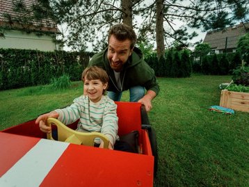 Mit Sicherheit ins Eigenheim – alles aus einer Hand Sorgloser Familienmoment mit Seifenkiste – Symbol für ganzheitliche Hausbau-Begleitung